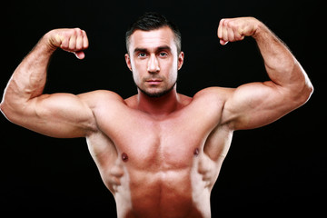 Fototapeta na wymiar Serious muscular man showing his biceps on black background