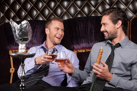 two young men smoke from shisha pipe.