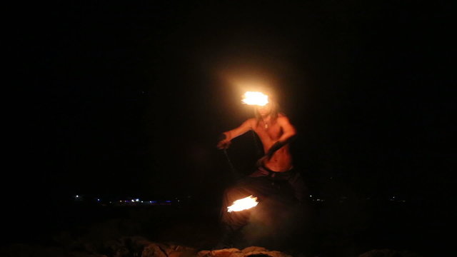 Male Artist of the spins fire poi on a rock 
