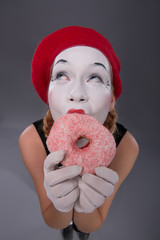 Portrait of pretty female mime eating a tasty pink donut isolate