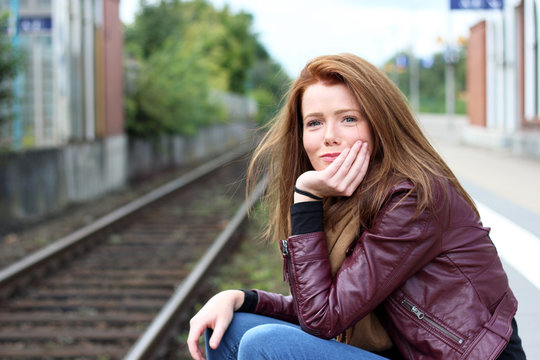 junge, freundliche Frau sitzt am Bahnhof