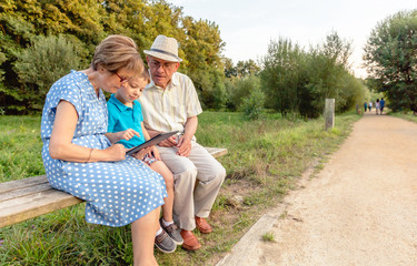 Naklejka na ściany i meble Grandchild and grandparents using a tablet outdoors