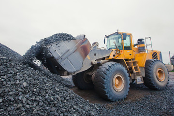 Yellow heavy excavator and bulldozer unloading road metal during