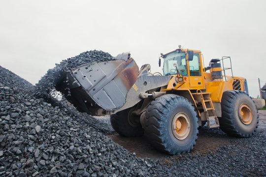 Yellow heavy excavator and bulldozer unloading road metal during
