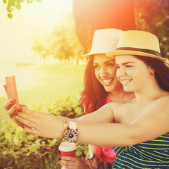 Two happy young women with hats taking a selfie in park