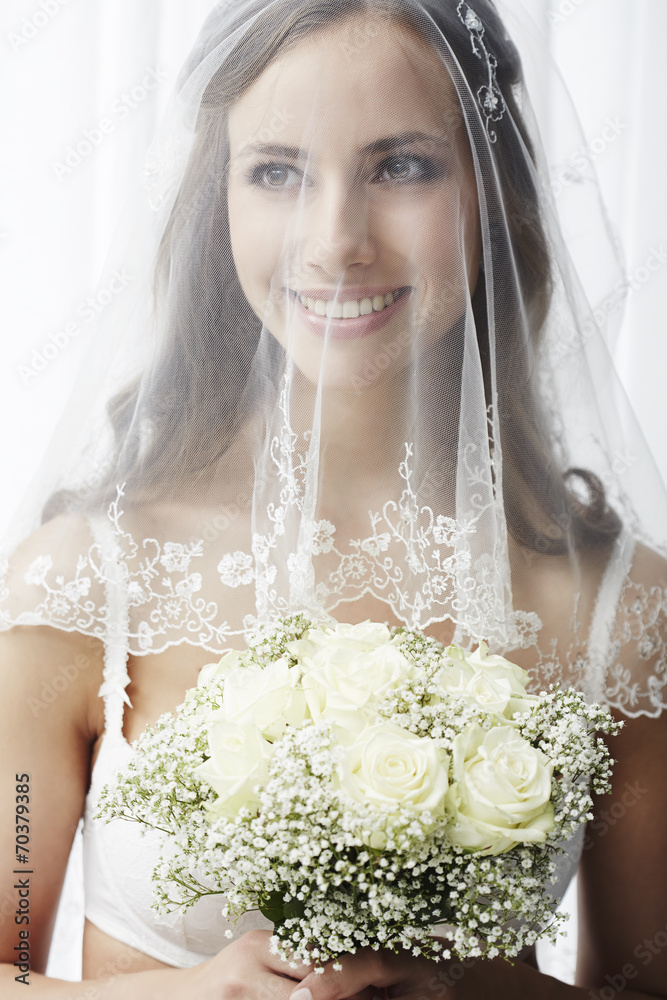 Wall mural Excited young bride in veil holding bouquet.