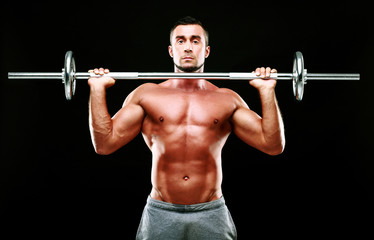 Fototapeta na wymiar Muscular man working out with barbell over black background