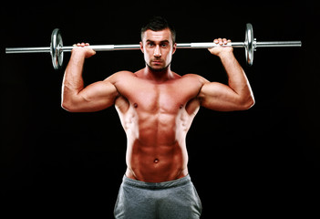 Muscular man doing exercise with barbell over black background