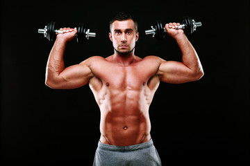 Fototapeta na wymiar Portrait of muscular man lifting dumbbells over black background