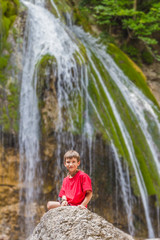 young happy smiling child boy on waterfall background