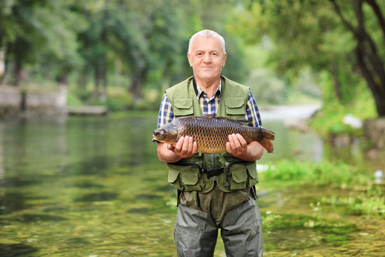Mature fisherman standing in river and holding fish