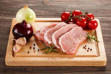 Raw pork chops on cutting board and vegetables
