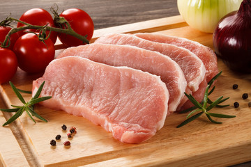 Raw pork chops on cutting board and vegetables