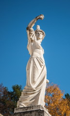 Antique sculpture in  autumn park on  background of blue sky