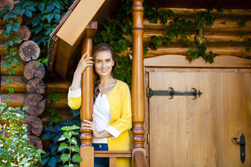 Happy young woman standing on the porch of a wooden house