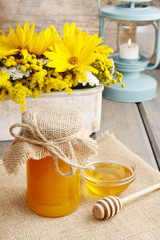 Jar of honey on wooden table, bouquet of sunflowers in the backg