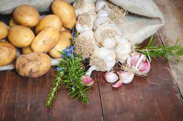 Fototapeta na wymiar Potatoes and garlic in canvas sack on rustic wooden table