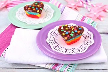Delicious rainbow cakes on plates, on color wooden background