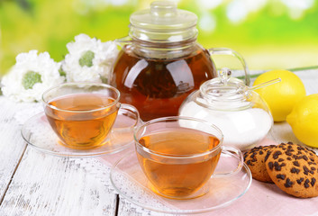 Teapot and cups of tea on table on bright background