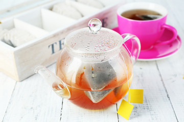 Cup of tea, teapot and tea bags on wooden table close-up