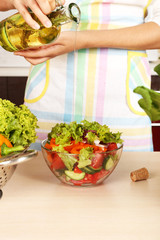 Fototapeta na wymiar Woman pouring olive oil in vegetable salad in kitchen
