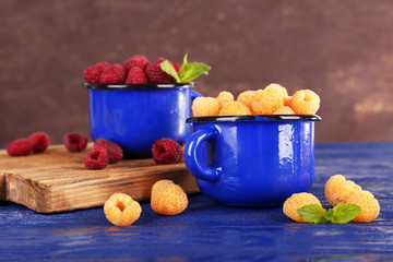 Red and yellow raspberries in dark blue metal mugs