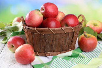 Sweet apples in wooden basket on table on bright background