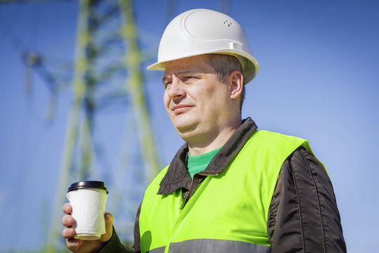 Engineer with coffee near high voltage towe