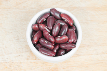 Kidney bean in white ceramic bowl on wood background.