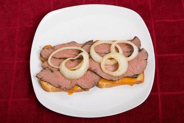 Hot Sliced Beef Sandwich with Onion Rings on Red Table