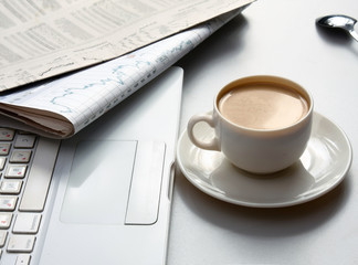 Cup of coffee near the laptop and newspapers