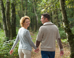 Fototapeta premium Happy couple holding hands and walking in the forest