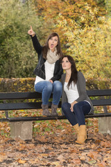Two beautiful lifestyle women on a bench in colorful autumn