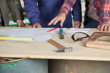 Carpenter Explaining Blueprint To Colleagues At Table