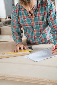 Carpenter Working On Blueprint While Measuring Wood
