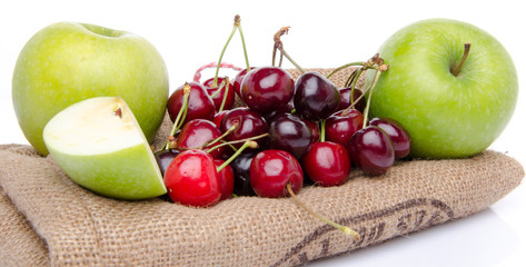 Ripe green apples and red cherries on a burlap