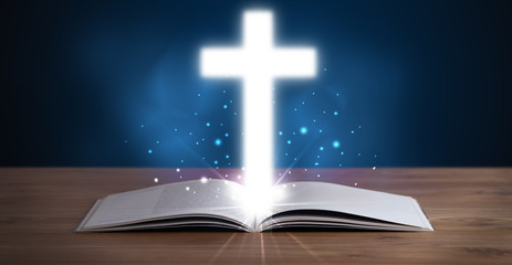 Open holy bible with glowing cross in the middle