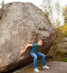 Man with backpack pushing a huge stone