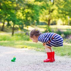 Beautiful little girl in red rain boots playing with rubber frog