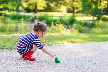 Beautiful little girl in red rain boots playing with rubber frog