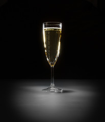 Glass of vine with bubbles on black background on light spot