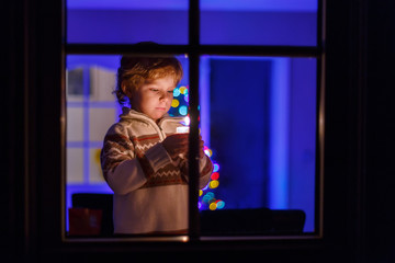 Sweet child standing by window at Christmas time and holding can