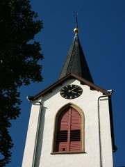 Kirchturmspitze mit Turmuhr der evangelisch-reformierten Kirche vor blauem Himmel im Sonnenschein...