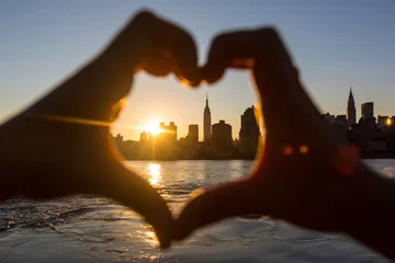 Poster Im Rahmen Heart Shaped Hands at Sunset, New York Skyline on Background © william87