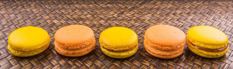 Yellow and orange colored French macarons on wicker background