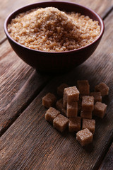 Brown sugar cubes and crystal sugar in bowl on wooden
