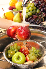 Woman's hands washing peaches and other fruits in colander in