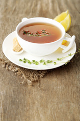 Cup of tasty herbal tea with thyme and lemon, on wooden table