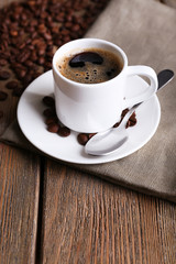 Cup of coffee and coffee beans on napkin on wooden background