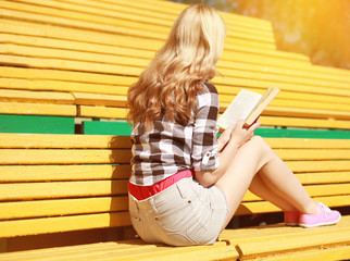 Young girl sitting reading a book on the bench in city park in s